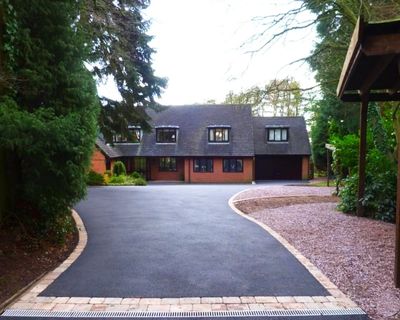 Entrée en asphalte résidentielle avec tracé courbé et bordures soignées, offrant une finition unifor