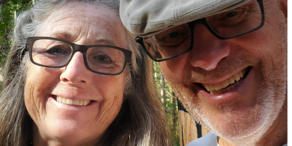 Smiling elderly couple wearing glasses outdoors on a sunny day.