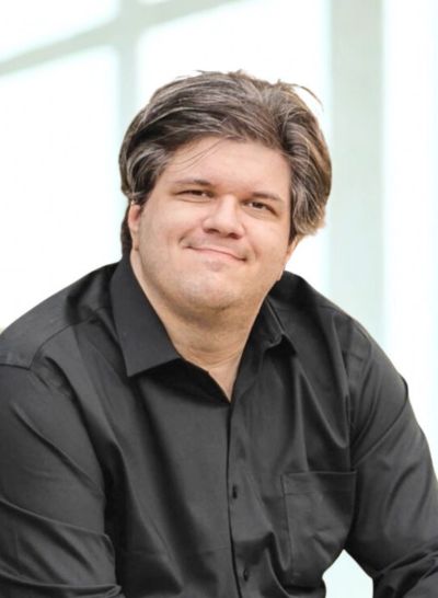 Man in a black shirt smiling gently against a bright background.