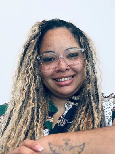 Smiling woman with long blonde dreadlocks and clear glasses.