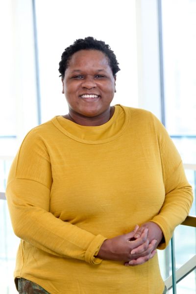 Smiling person in a mustard yellow sweater posing indoors.