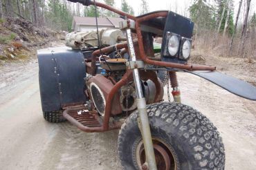 Rusty homemade trike with large tires on a gravel road.