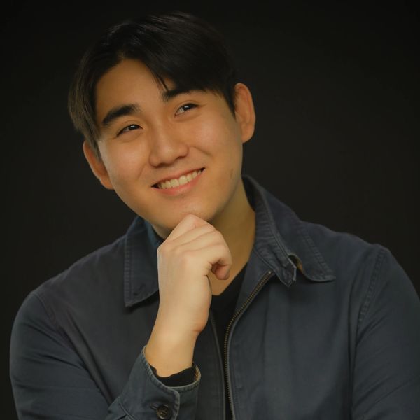 Smiling young man posing thoughtfully against dark background.