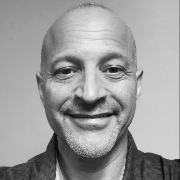 Smiling bald man with goatee in black and white portrait.