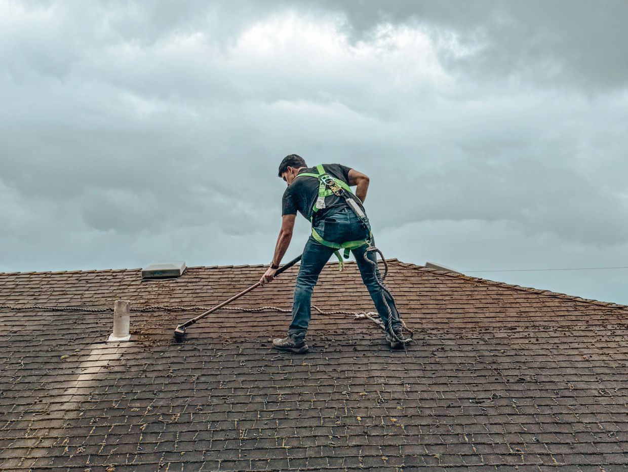 Man cleaning a rooftop with a brush and safety harness.