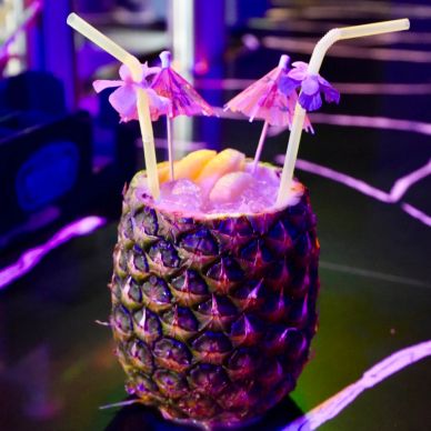 Tropical drink served in a hollowed pineapple with straws and paper umbrellas.