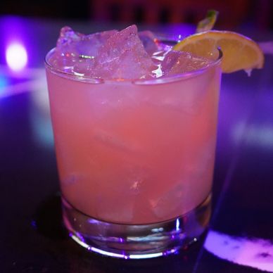 Pink cocktail with ice and lemon wedge.
