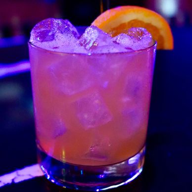 A vibrant cocktail with ice and an orange slice garnish.