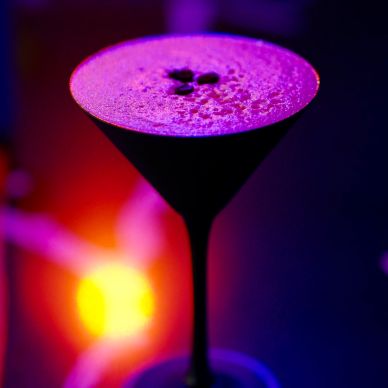 Cocktail in a black martini glass with purple foam and coffee beans.
