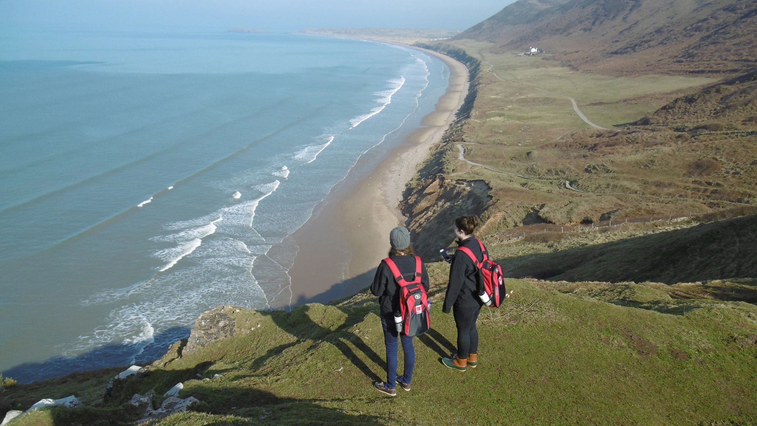Two people standing atop a cliff overlooking a shoreline.