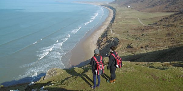 Two people standing atop a cliff overlooking a shoreline.