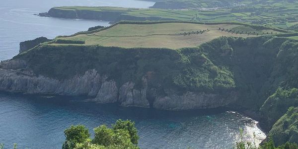 A large grassy field, ending in a cliff leading down to water