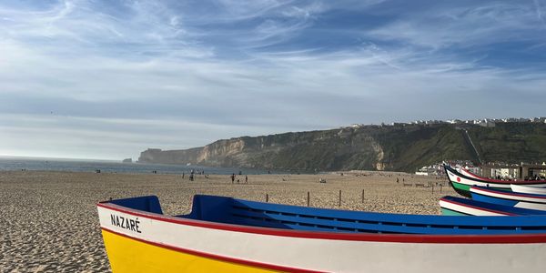 A yellow, white, and blue boat, sitting on a large sandy beach.