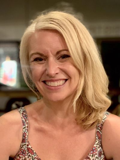 Smiling blonde woman with styled hair in a patterned dress.