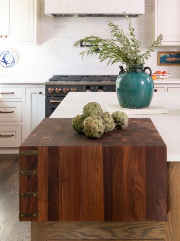 Artichokes on a wooden counter with a vase in background.