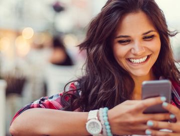 Young woman smiling while looking at her phone outdoors.