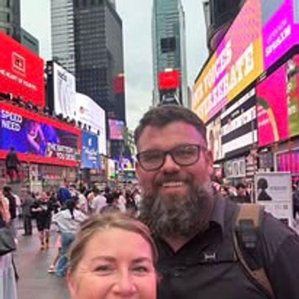 Smiling couple posing in a busy Times Square filled with bright billboards.
