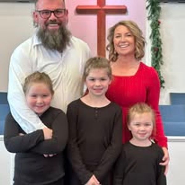 Family of five smiling in a church with a cross in the background.