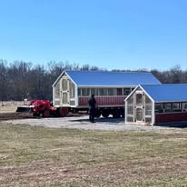 Two large chicken coops being moved by a tractor in a field.