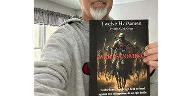 A man holding a book titled 'Twelve Horsemen: War is Coming' indoors.