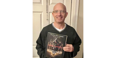 Man smiling and holding a book titled 'Twelve Horsemen'.