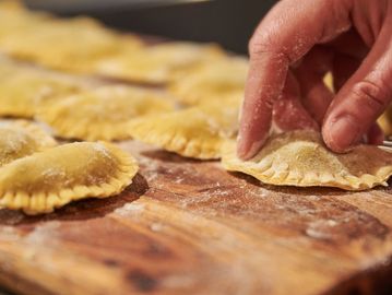 Close-up of hand-shaped ravioli being formed on a floured wooden surface.
