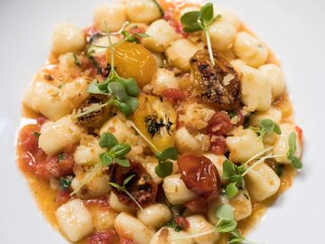 Pan-seared gnocchi served with blistered tomatoes, microgreens, and light tomato sauce.
