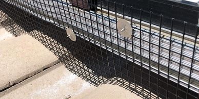 Wire mesh attached to a window frame with washers and screws.