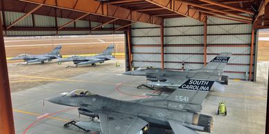 Military fighter jets parked inside and outside a hangar.