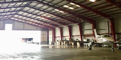 Small airplane parked inside a spacious hangar with bright light outside.