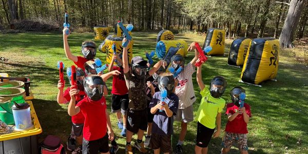 Kids posing with paintball guns and masks outdoors.