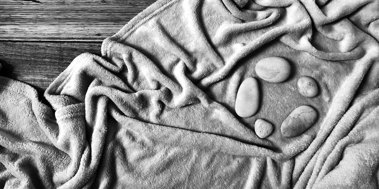 Black and white image of a circle of stones on a blanket on floorboards. 
