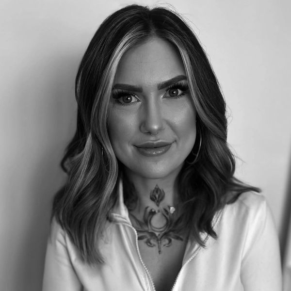 Black and white portrait of a woman with wavy hair and a chest tattoo.