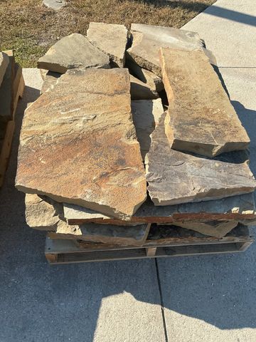 Stack of large, flat natural stone slabs on a wooden pallet outdoors.