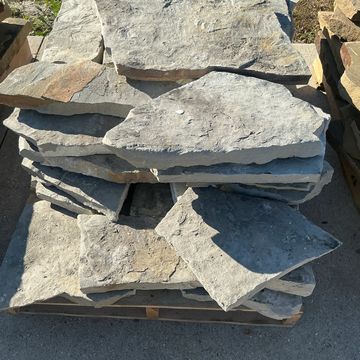 Stack of large flat stones on a wooden pallet outdoors.