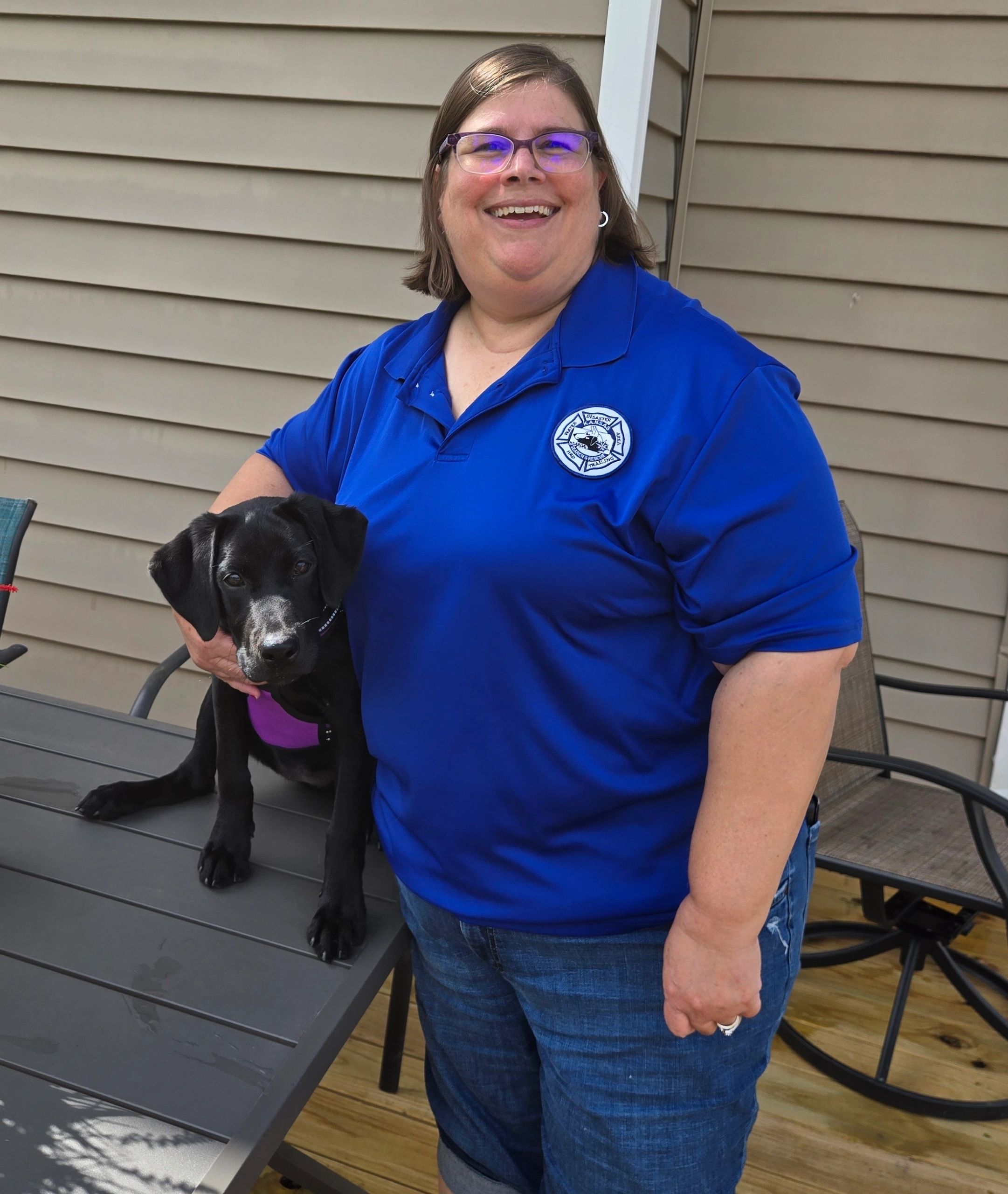 Smiling woman in blue shirt holding a black puppy.