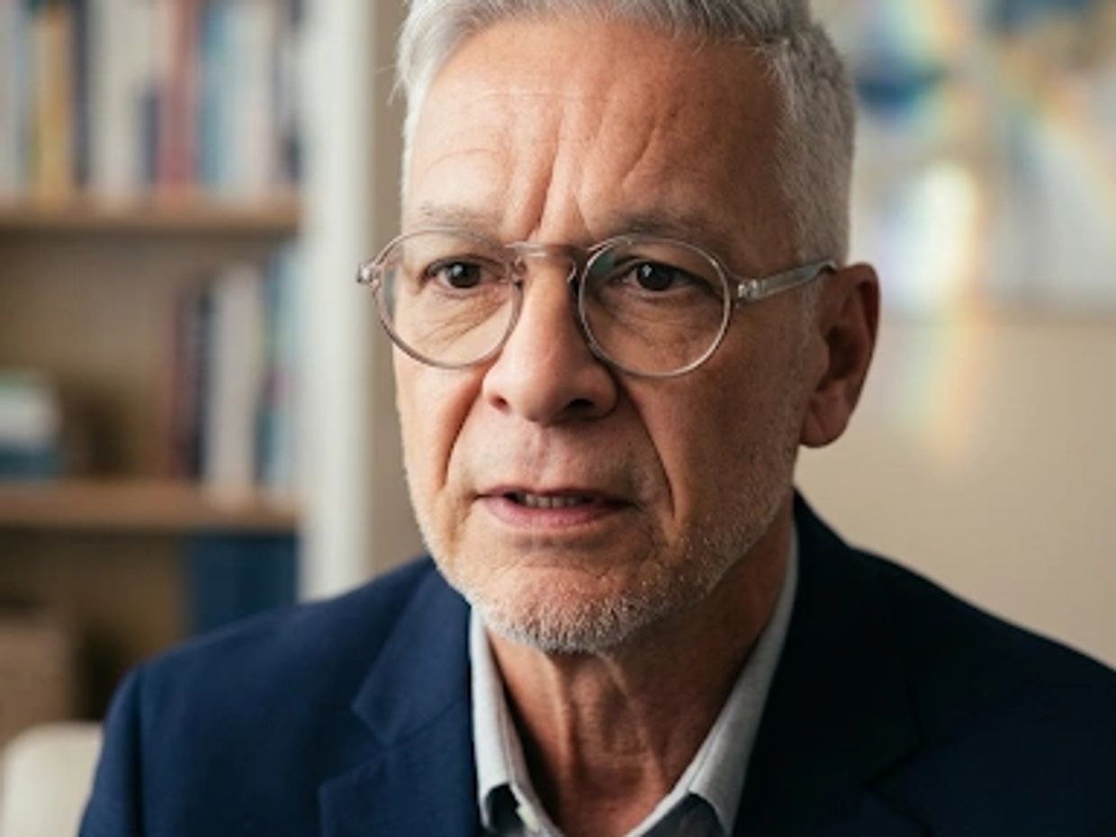 Elderly man wearing glasses and a suit jacket.