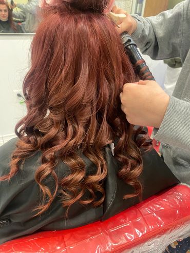 A person curling another's long red hair.