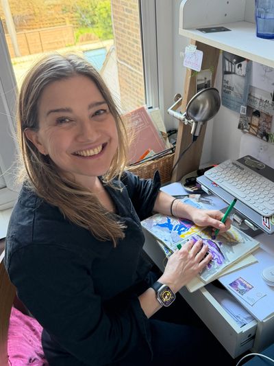 Smiling woman painting at her desk by the window.