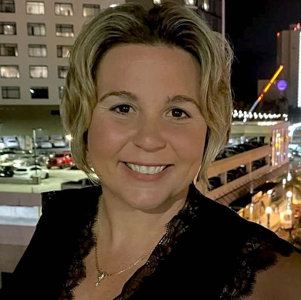 Smiling woman with short blonde hair wearing a black lace top at night.