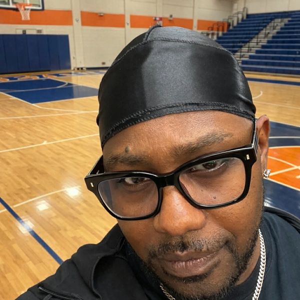 Man wearing glasses and a black durag in a basketball gym.