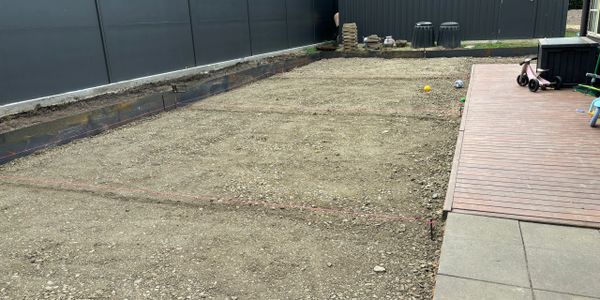 A backyard with leveled dirt and some scattered toys, adjacent to a wooden deck.