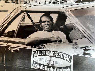 Man sitting in car holding Hall of Fame Festival sign.