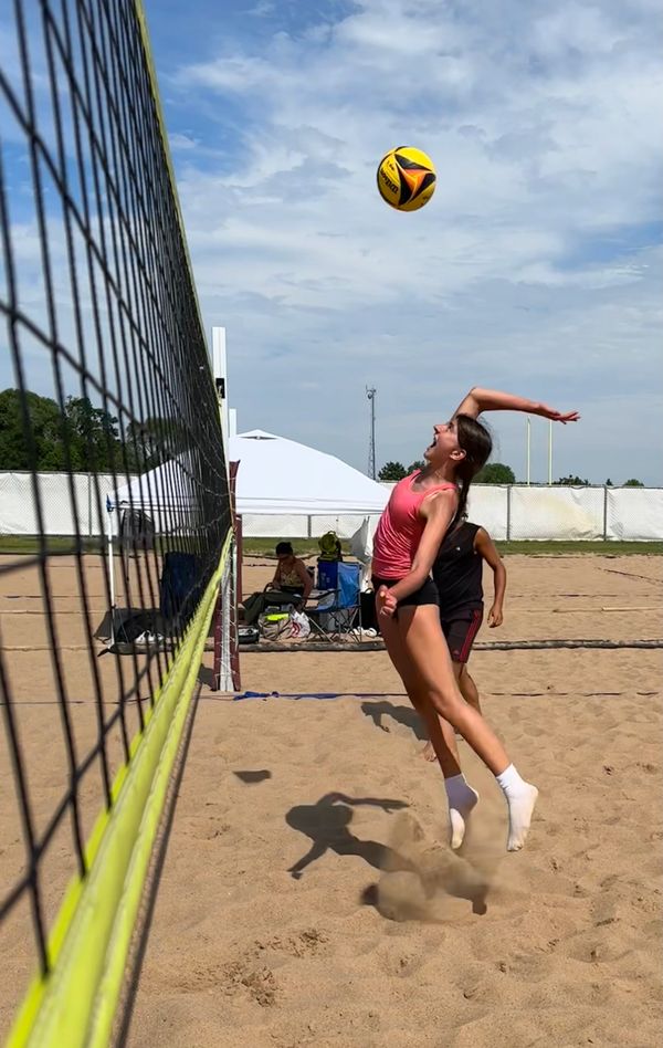 Athlete jumping to hit a volleyball over the net on a sunny beach court.