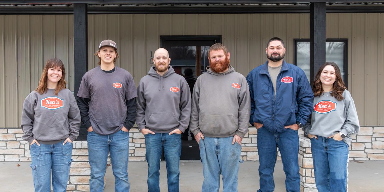 Group of six smiling people wearing matching Ken's branded clothing standing outside.