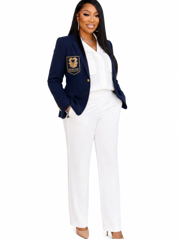 Confident woman in a navy blazer and white outfit posing with hands in pockets.