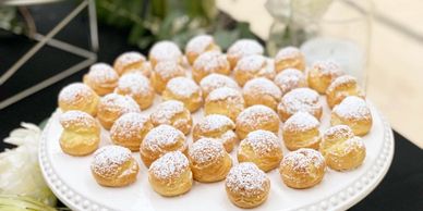 Elegant Cream Puffs with a Dusting of Powdered Sugar displayed on a round platter.