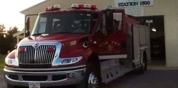 A red fire truck parked outside a fire station at dusk.