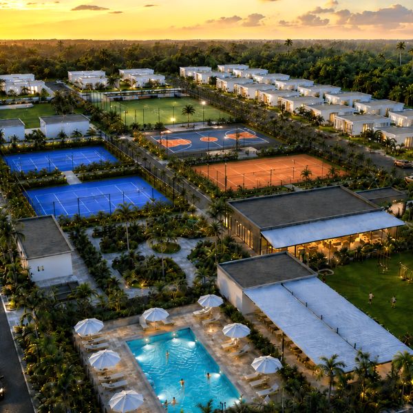 Aerial view of a luxury resort with pools, tennis courts, and villas at sunset.