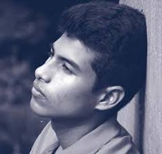 Black and white portrait of a young man leaning against a wall, gazing thoughtfully.